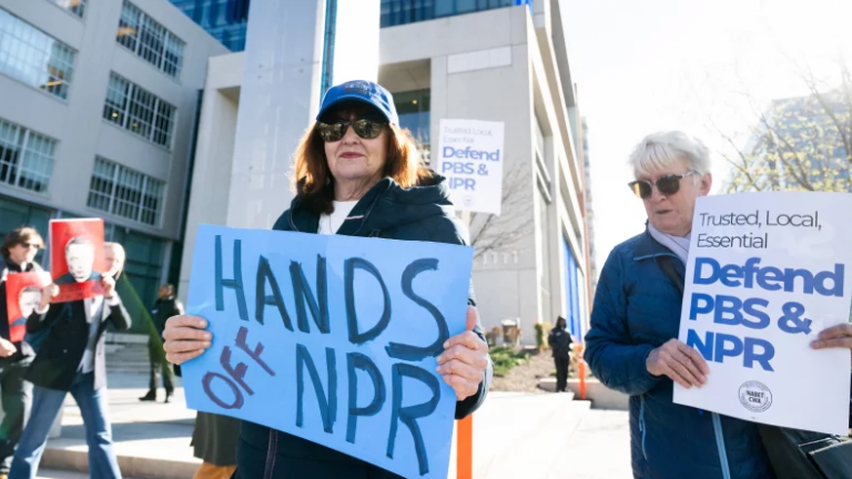 Protestors hold signs supporting funding for NPR